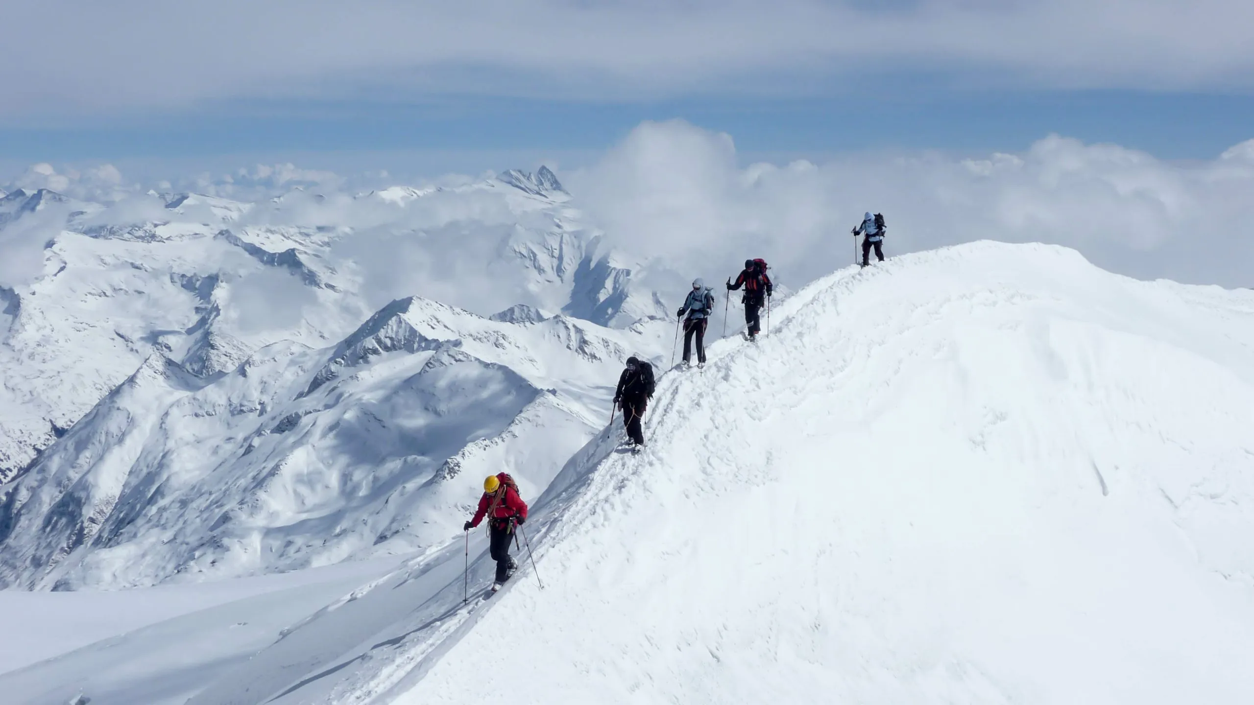 horský vůdce a jeho klienti na exponovaném vrcholovém hřebeni během zimního výstupu v rakouských Alpách.