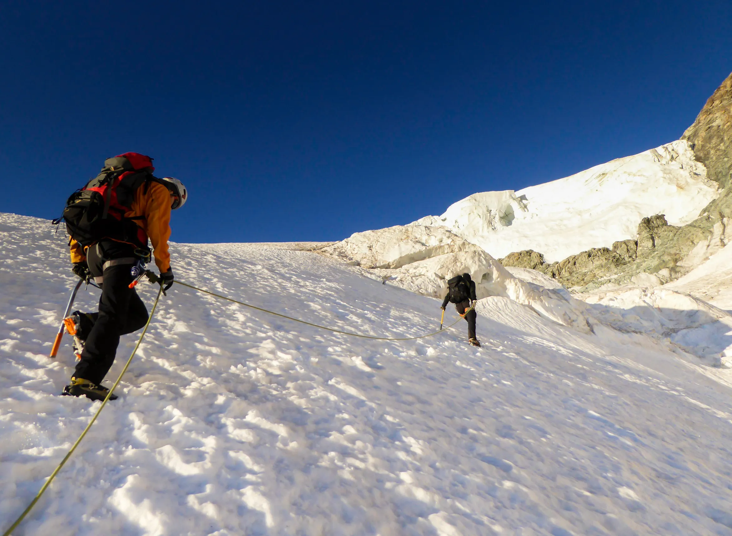 dva horolezci na laně při přechodu a výstupu po strmém ledovci v národním parku Barre des Ecrins ve francouzských Alpách.