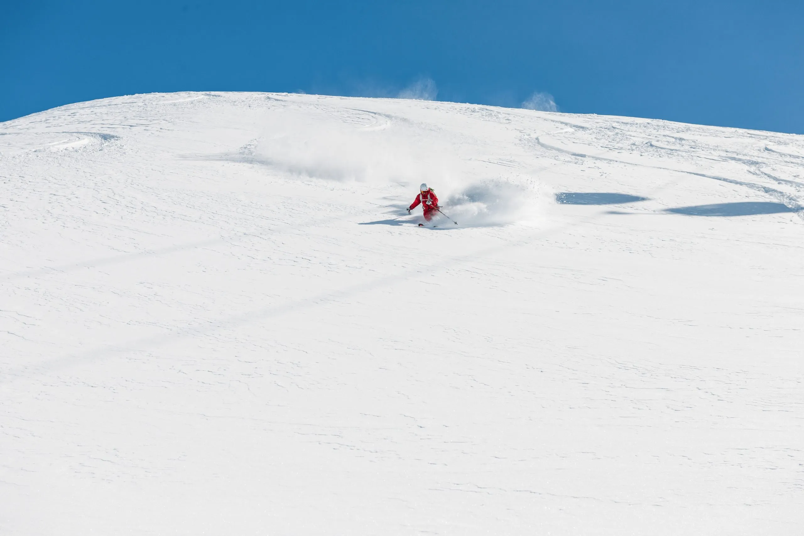 Freeride-Skifahrer fährt schnell bergab. Archivbild eines Freeride-Skifahrers, der in tiefem Pulverschnee schnell bergab fährt. Im Hintergrund ist ein schöner, blauer Himmel zu sehen. Der Standort ist Hochgurgl